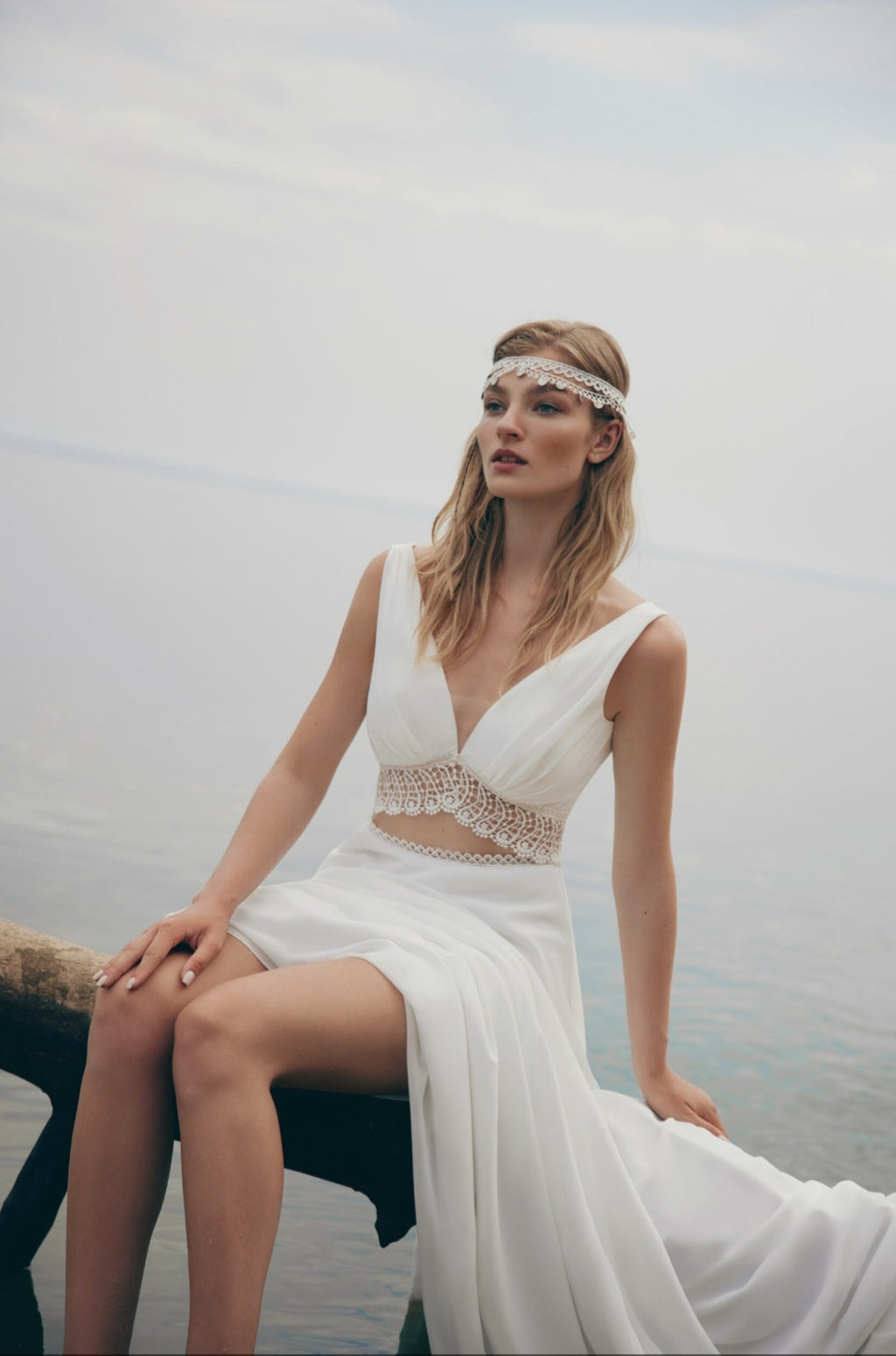 Woman in a white wedding dress sitting by a body of water.