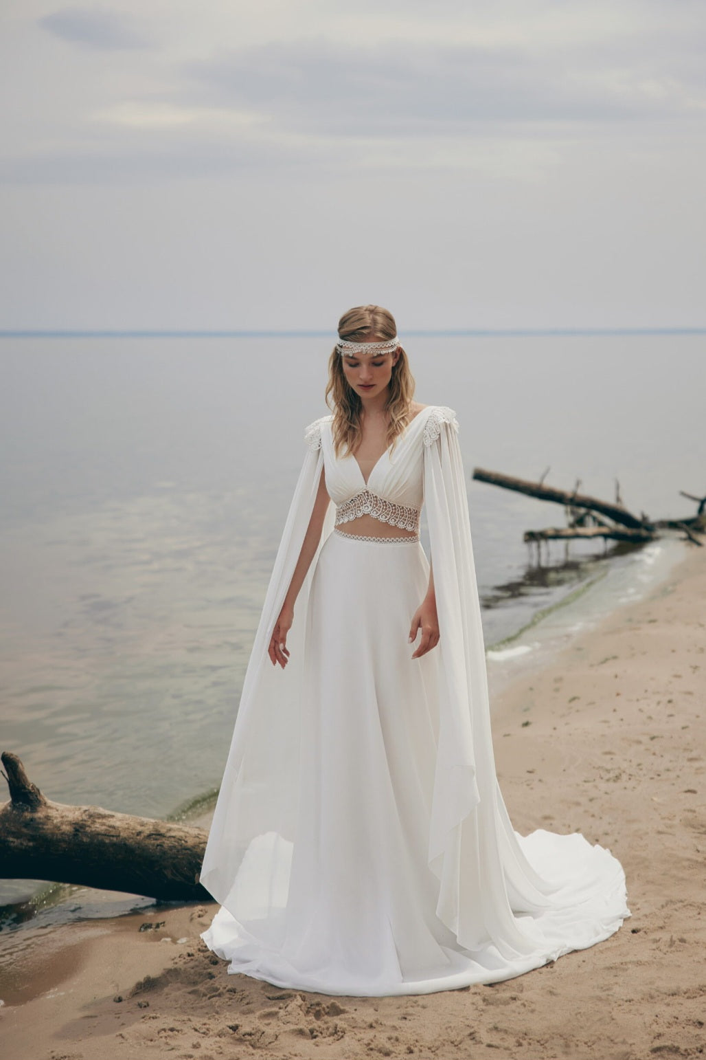Woman in a white bridal gown standing on a beach with a calm sea in the background