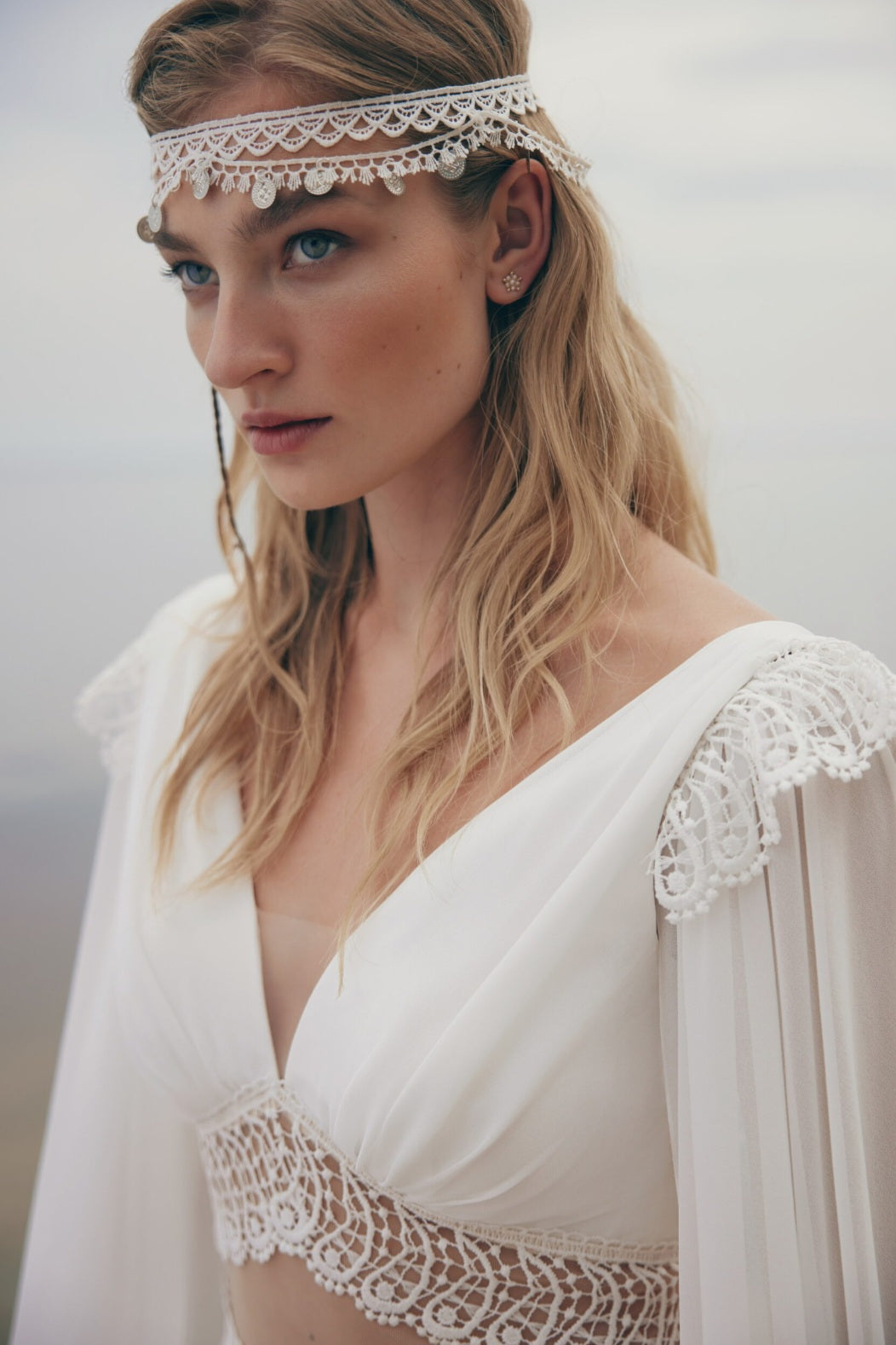 Woman wearing a white lace dress with a matching headband against a neutral background