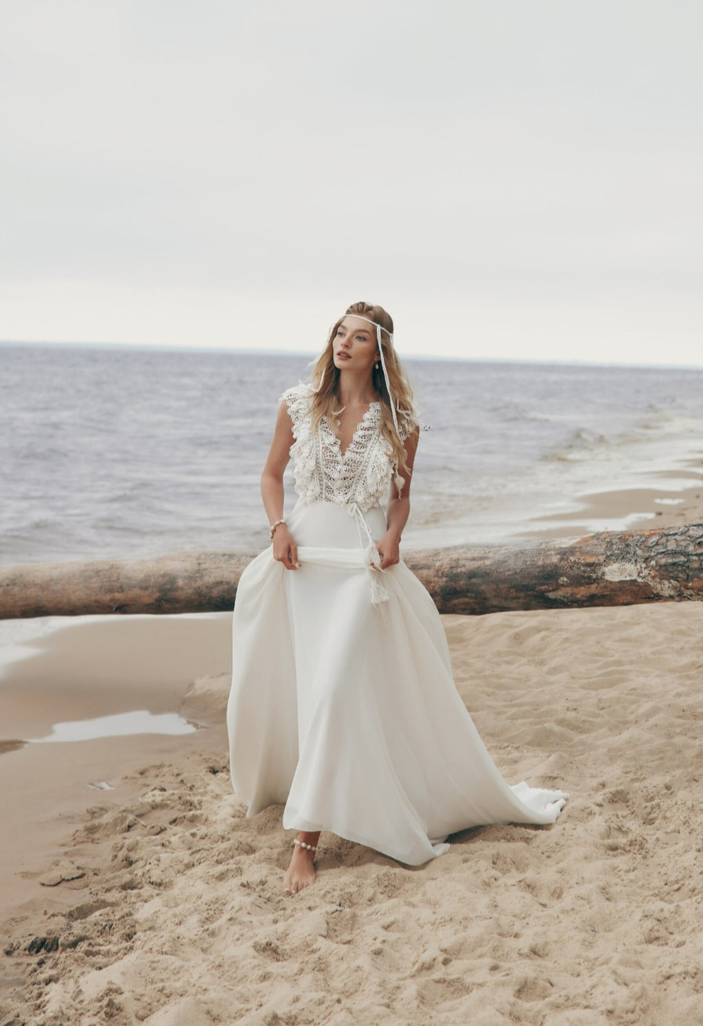 Woman in a white wedding dress standing on a beach with ocean in the background