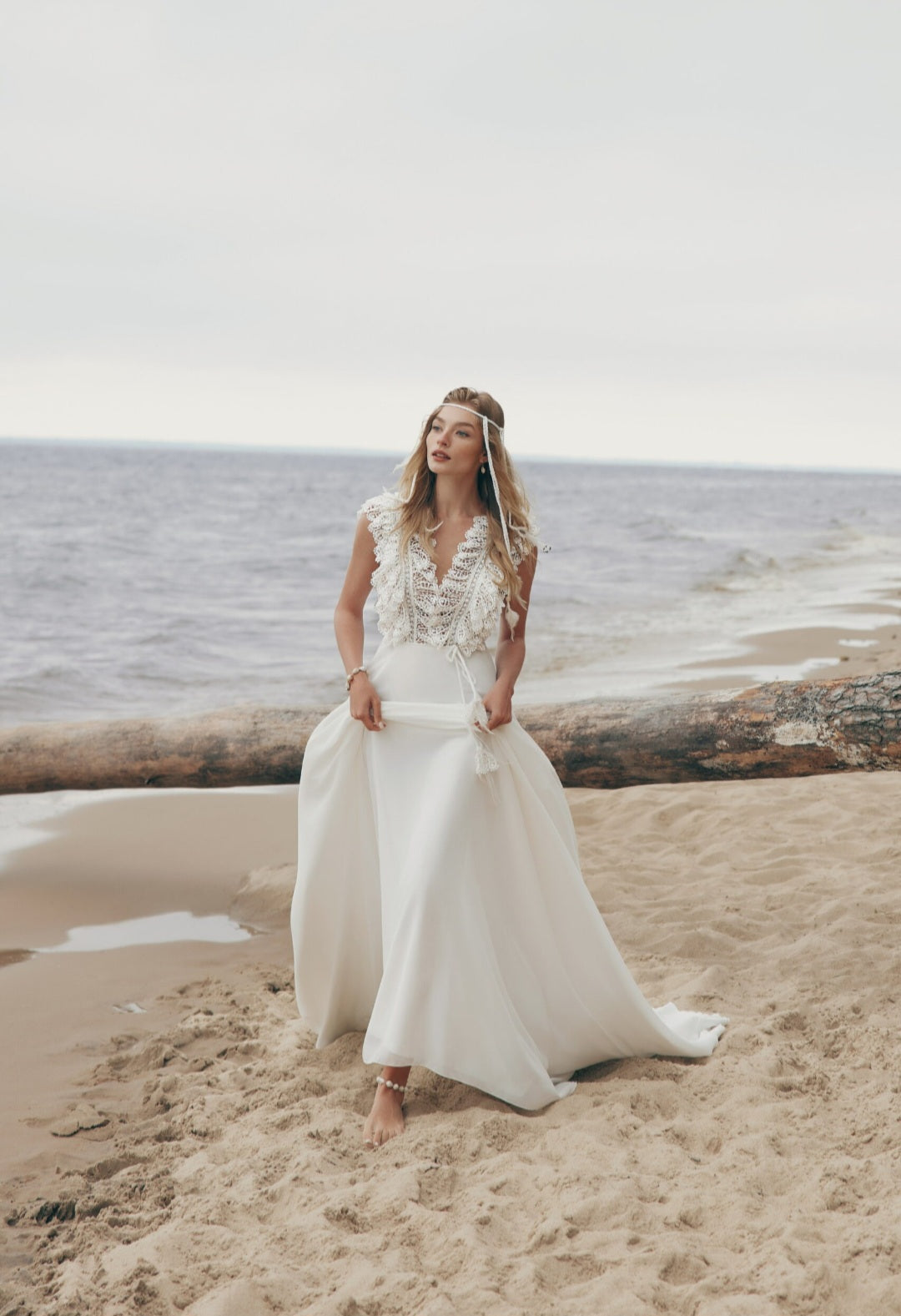 Woman in a white wedding dress standing on a beach with ocean in the background