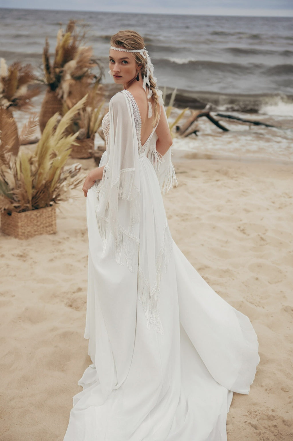 Woman in a white dress standing on a beach with driftwood and ocean in the background