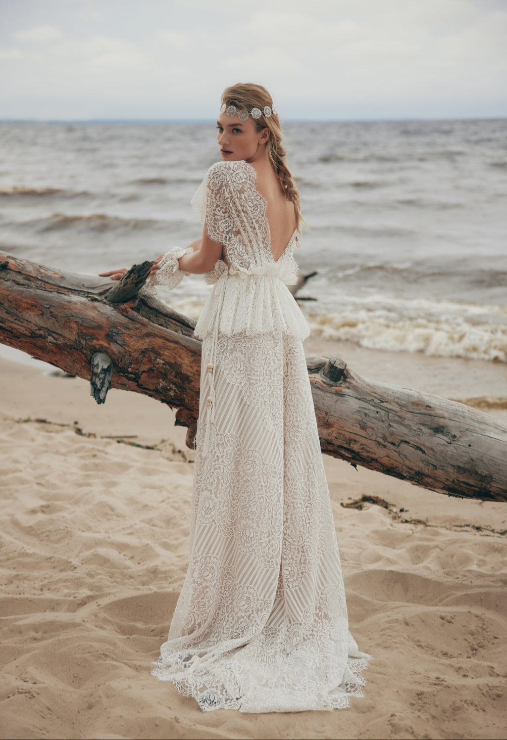 Woman in a lace dress standing on a beach with ocean in the background