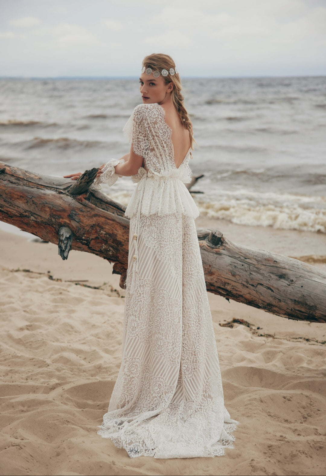 Woman in a lace dress standing on a beach with ocean in the background