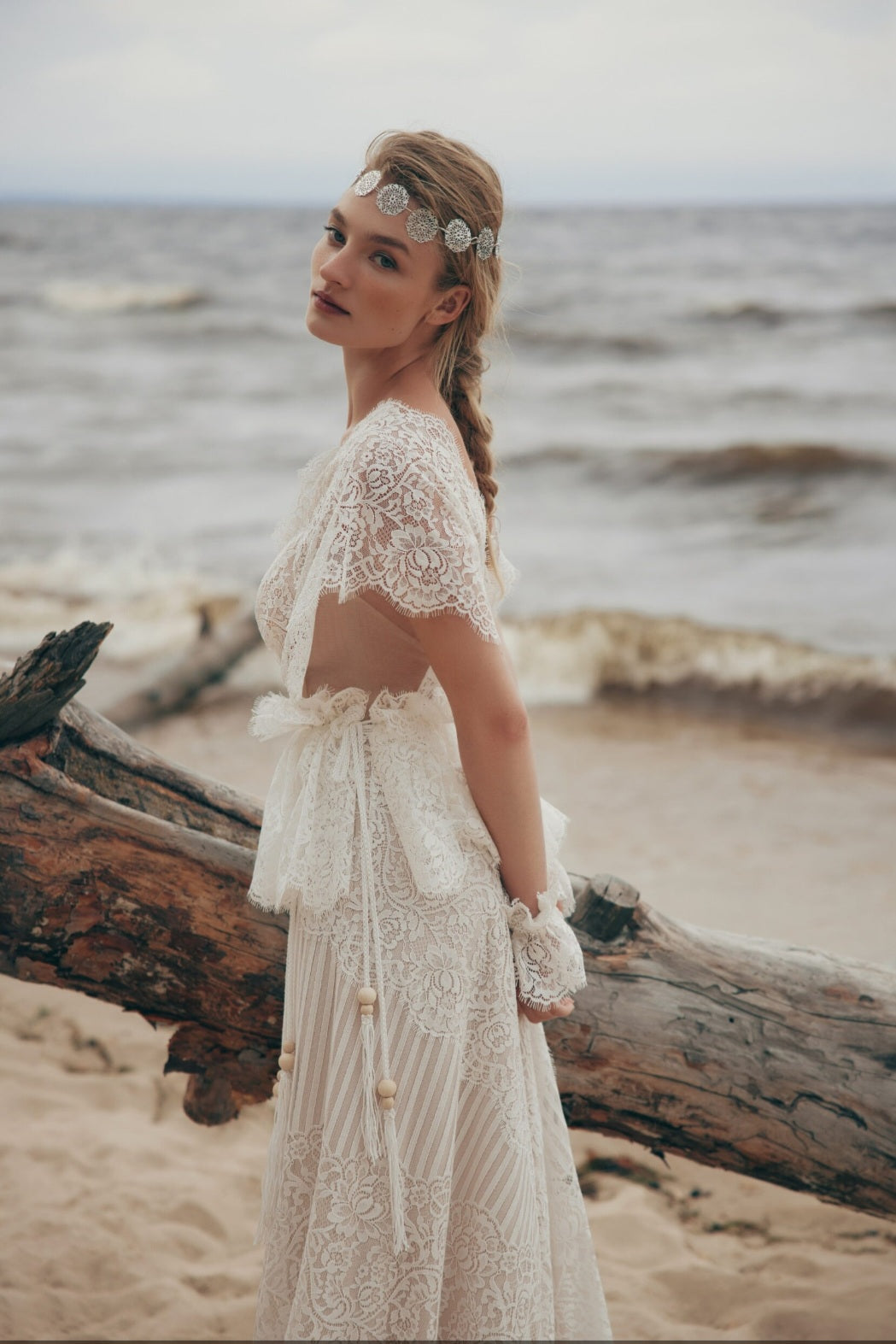 Woman in a lace dress standing on a beach with ocean in the background