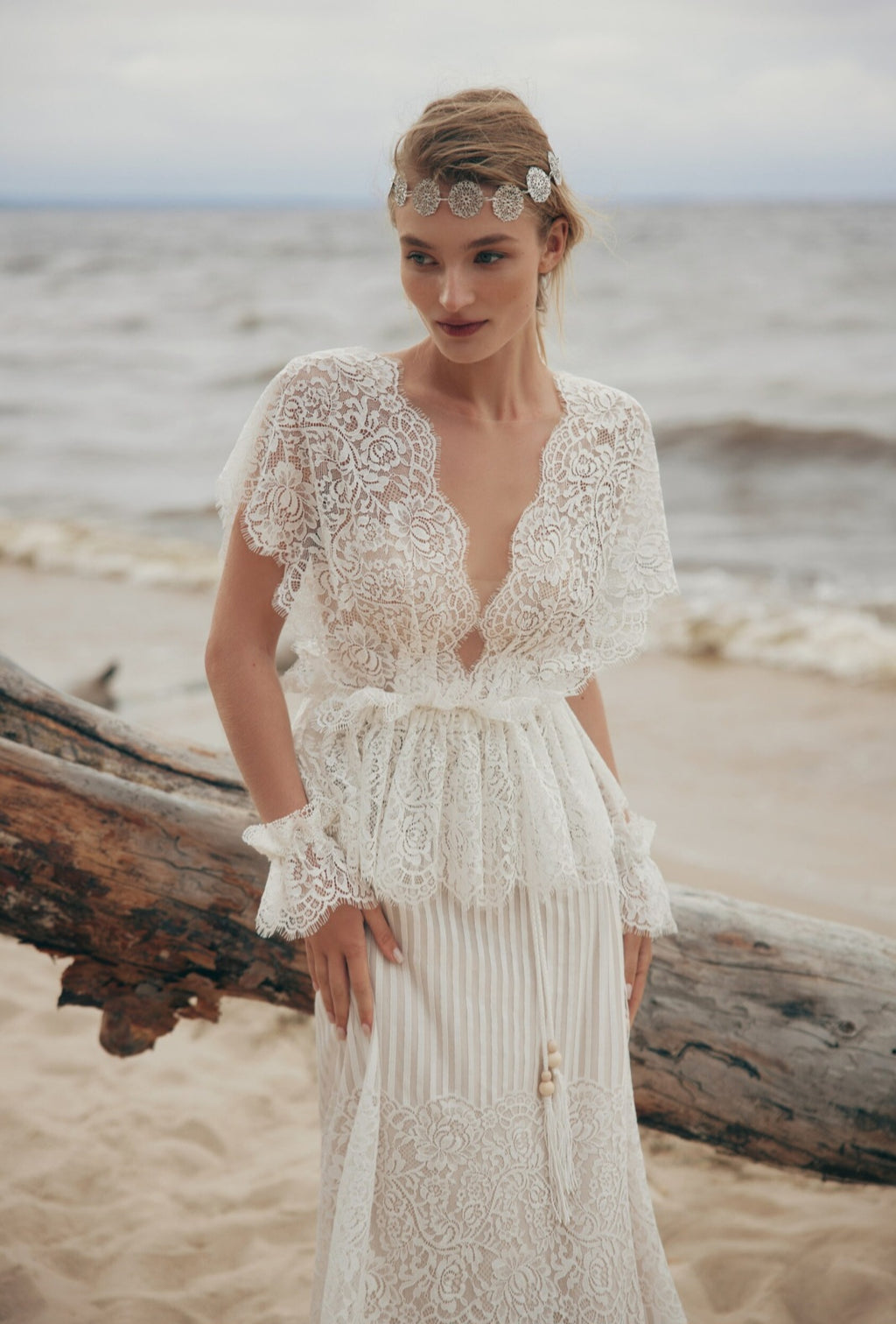 Woman in a lace wedding dress standing on a beach with ocean in the background