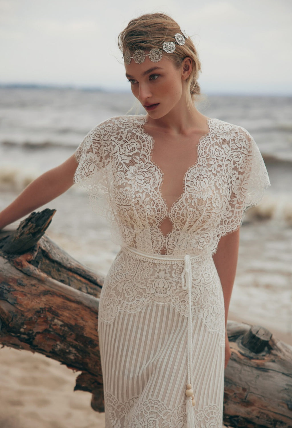 Woman in a lace wedding dress standing on a beach with ocean in the background