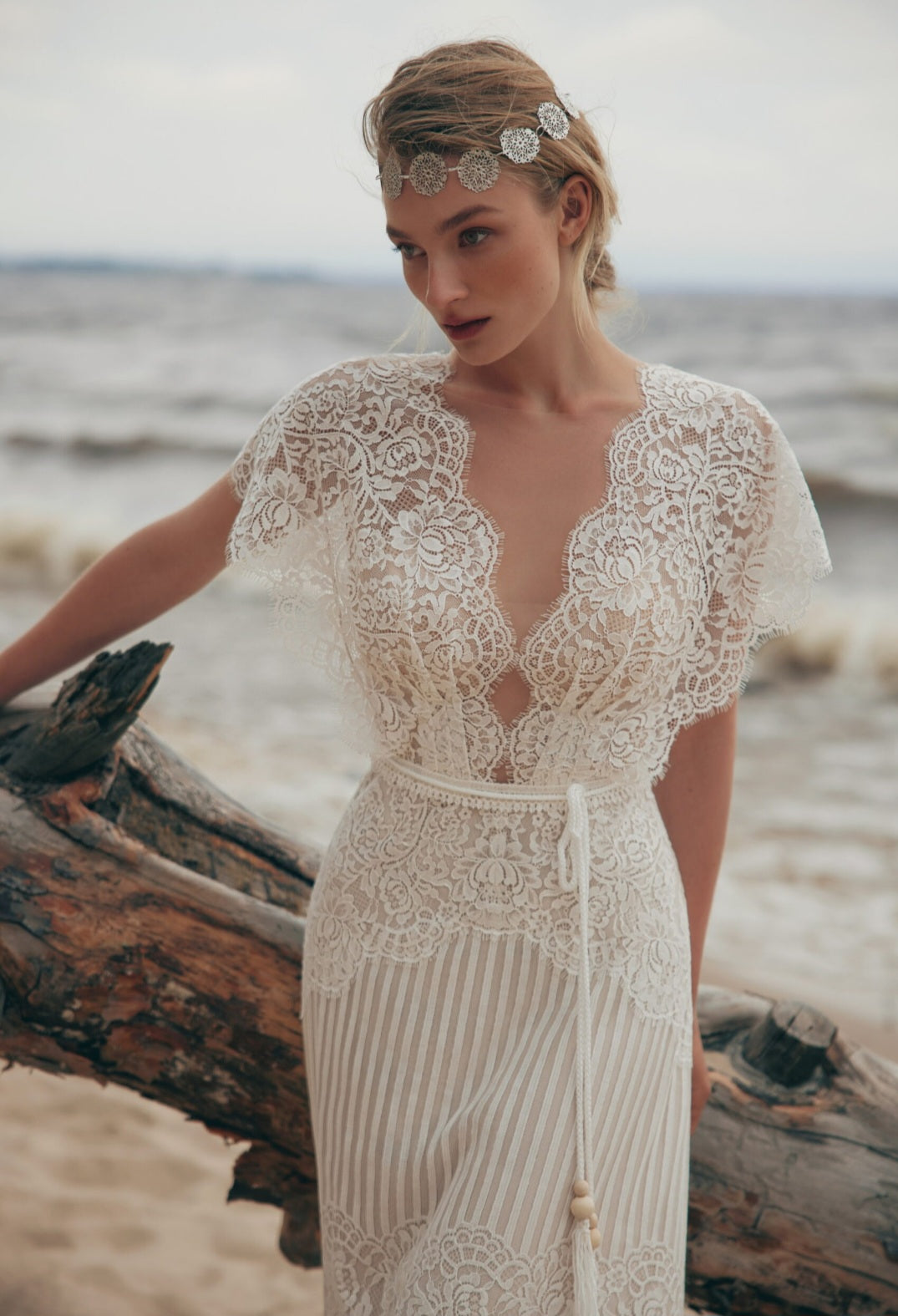 Woman in a lace wedding dress standing on a beach with ocean in the background