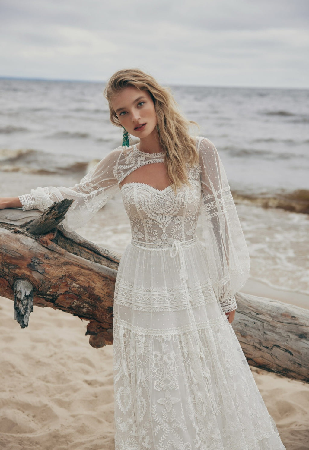 Woman in a lace dress standing on a beach with ocean in the background