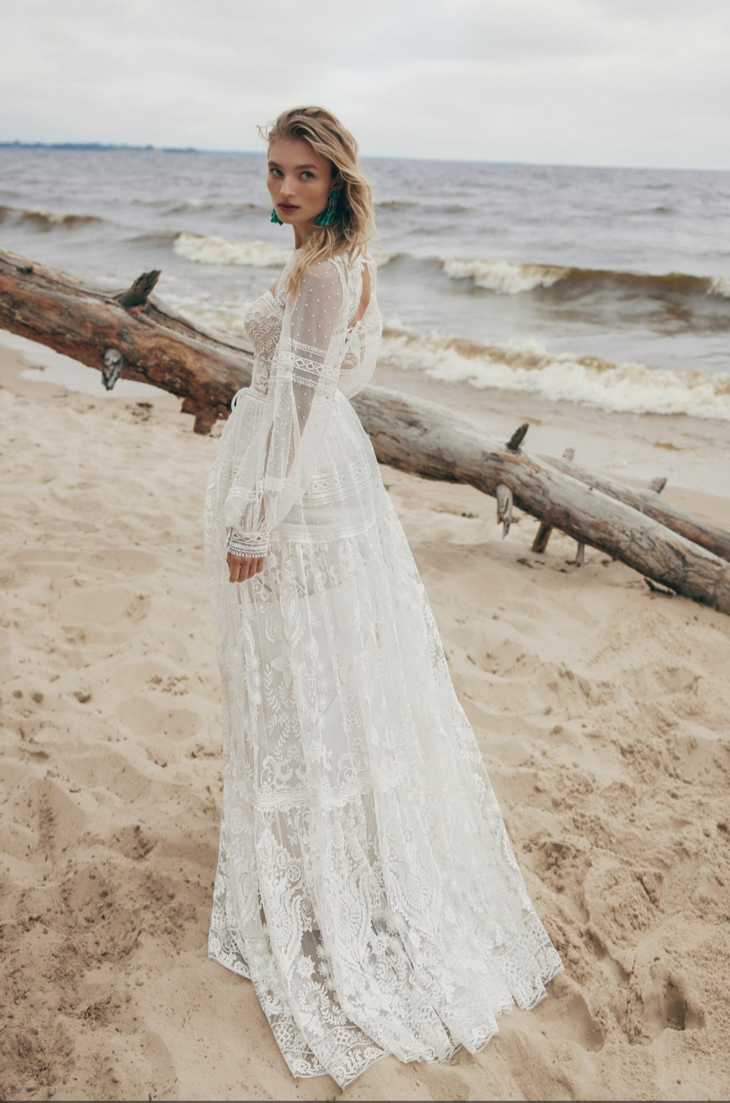 Woman in a white lace dress standing on a beach with ocean waves in the background