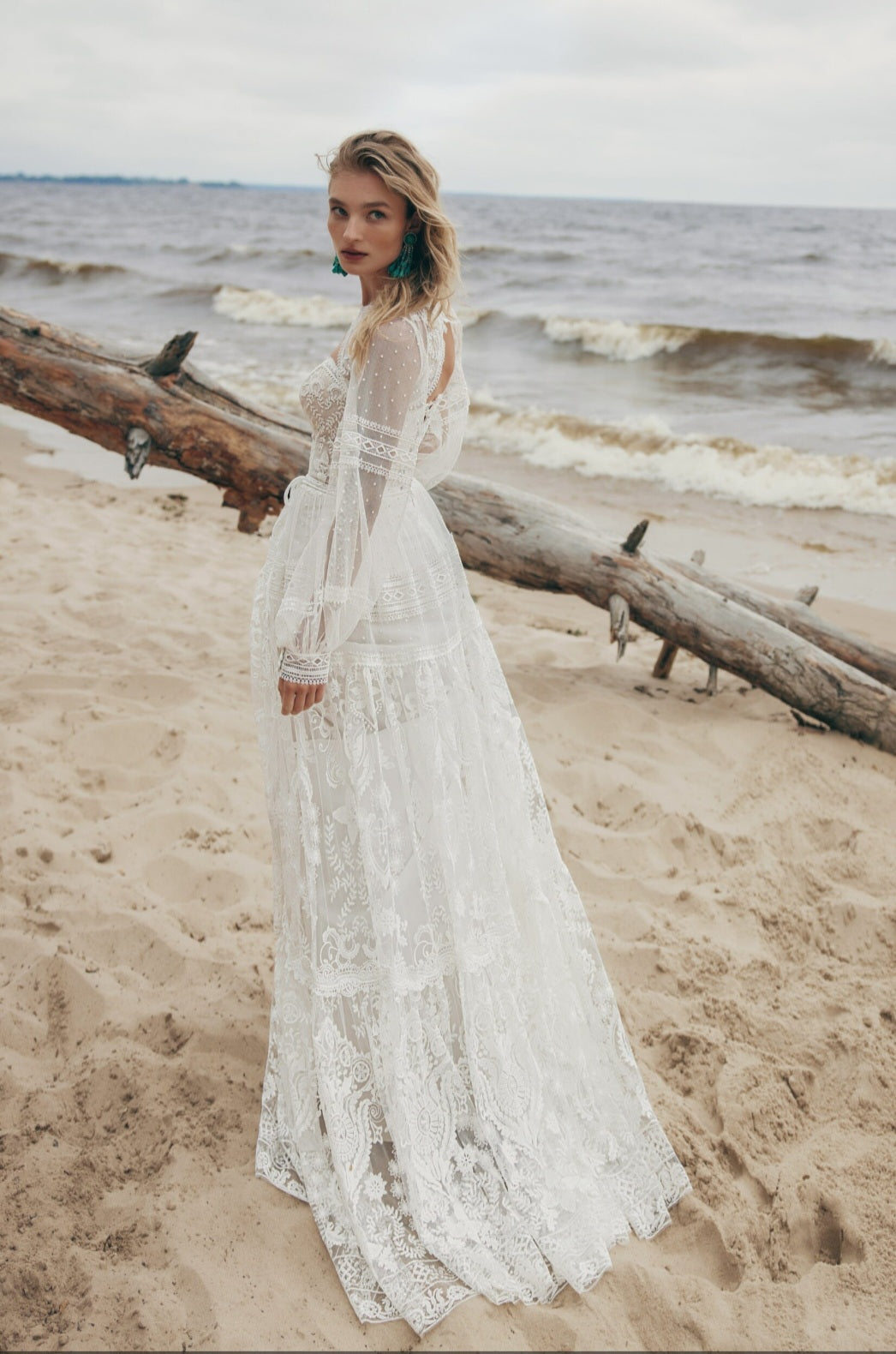 Woman in a white lace dress standing on a beach with ocean waves in the background