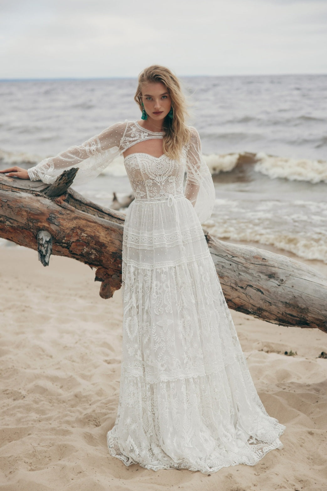 Woman in a white lace dress standing on a beach with ocean waves in the background