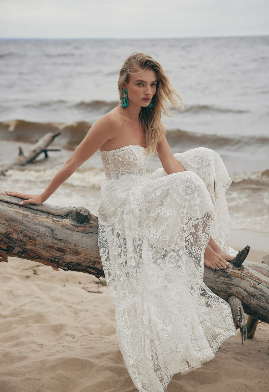 Woman in a white lace dress sitting on a log by the ocean