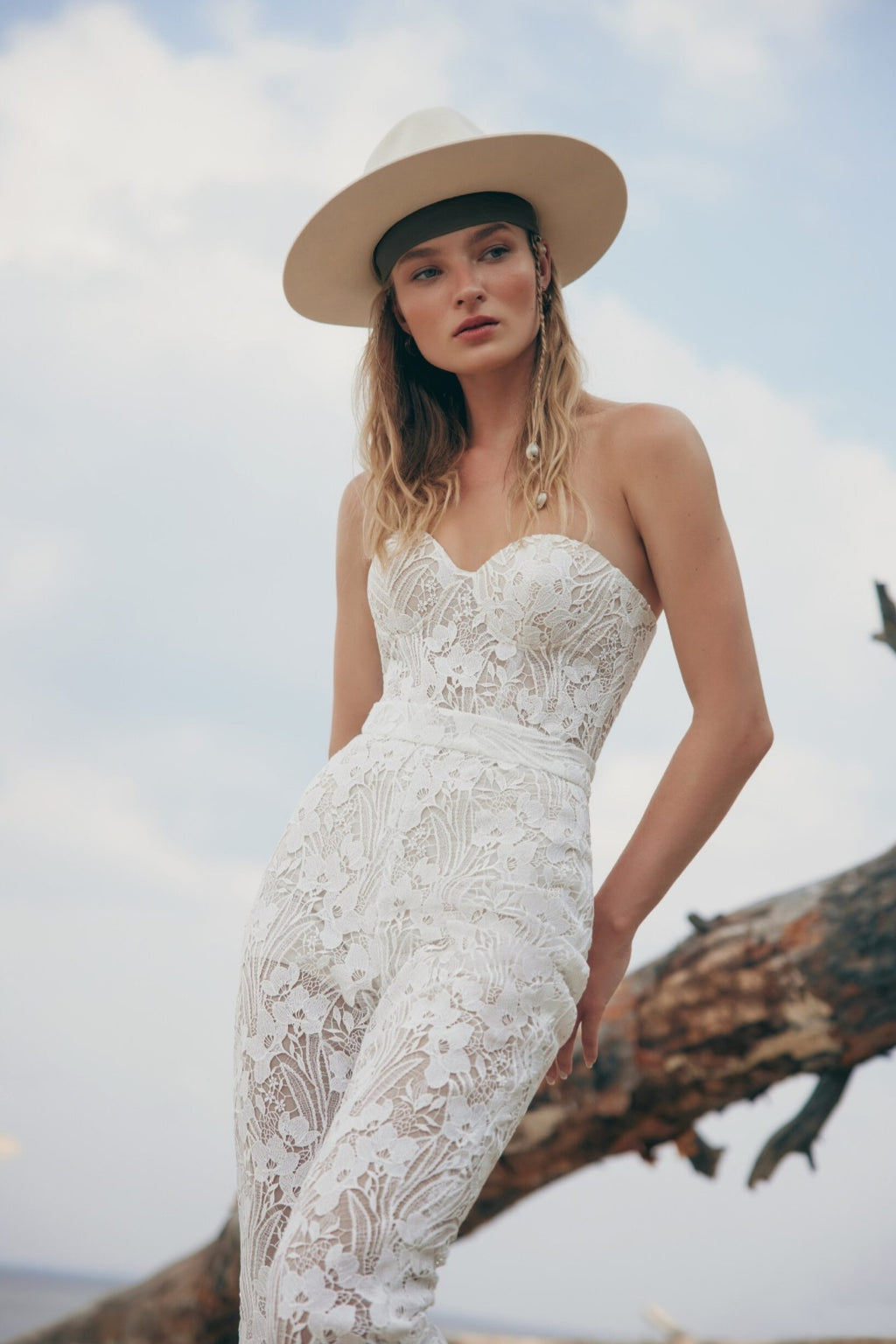 Woman in a white lace dress and hat standing on a beach with a blurred background