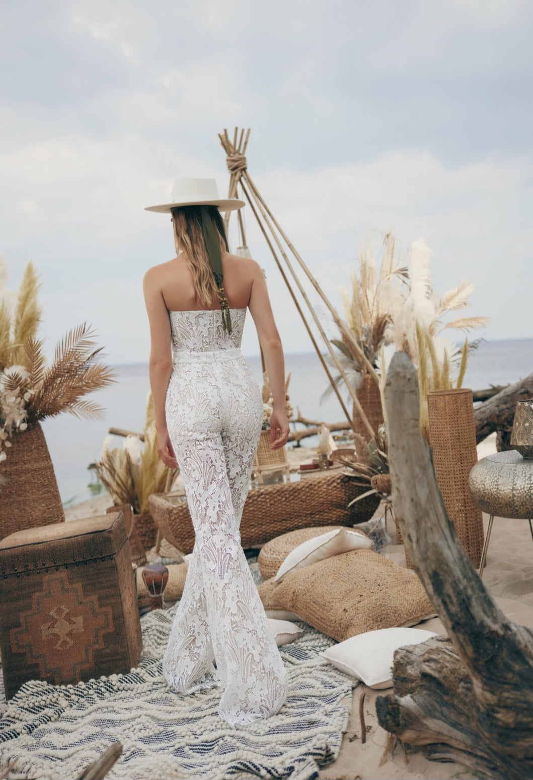 Woman in a white lace dress standing in a coastal setting with ocean view.