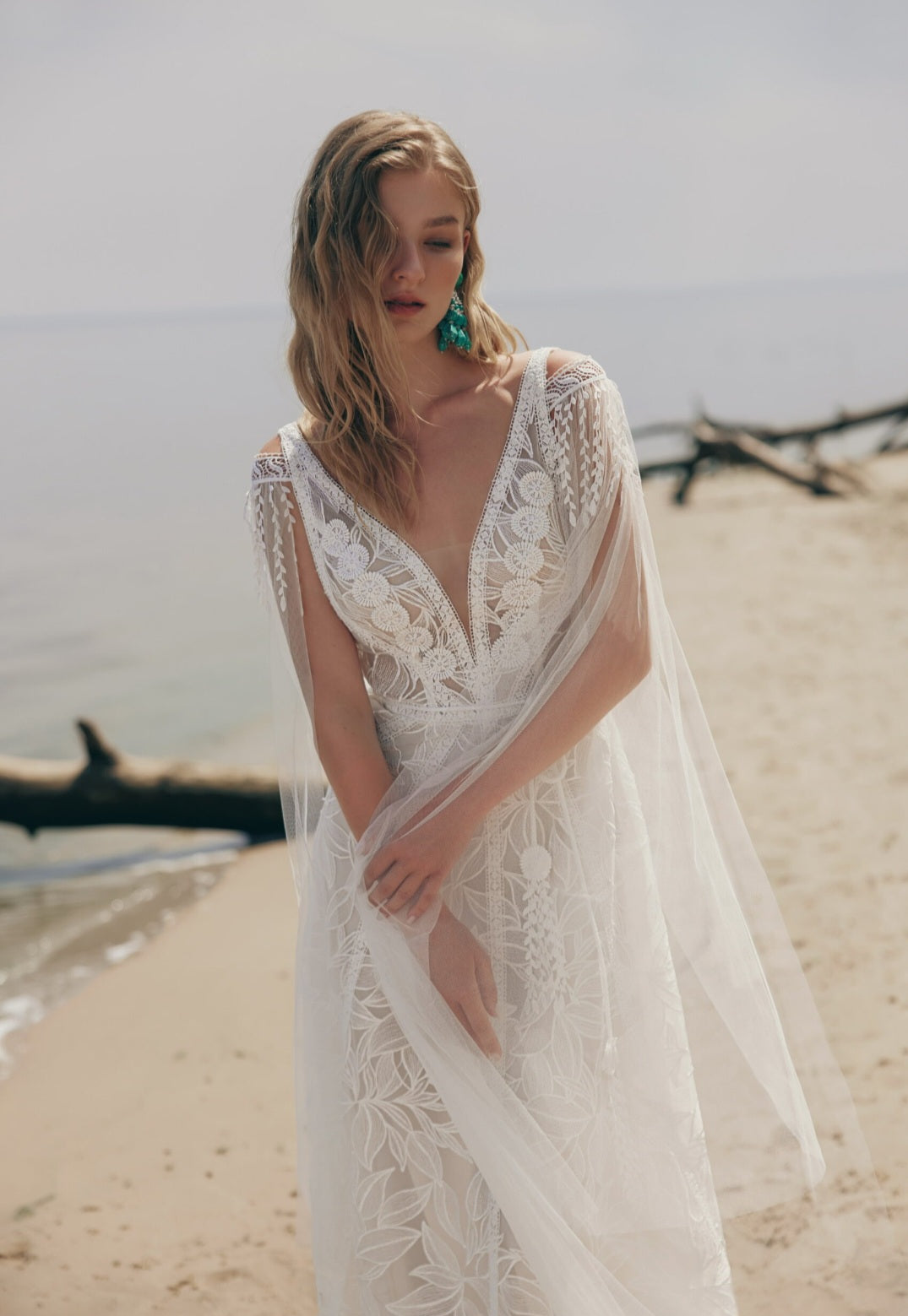 Woman in a lace dress standing on a beach with ocean in the background