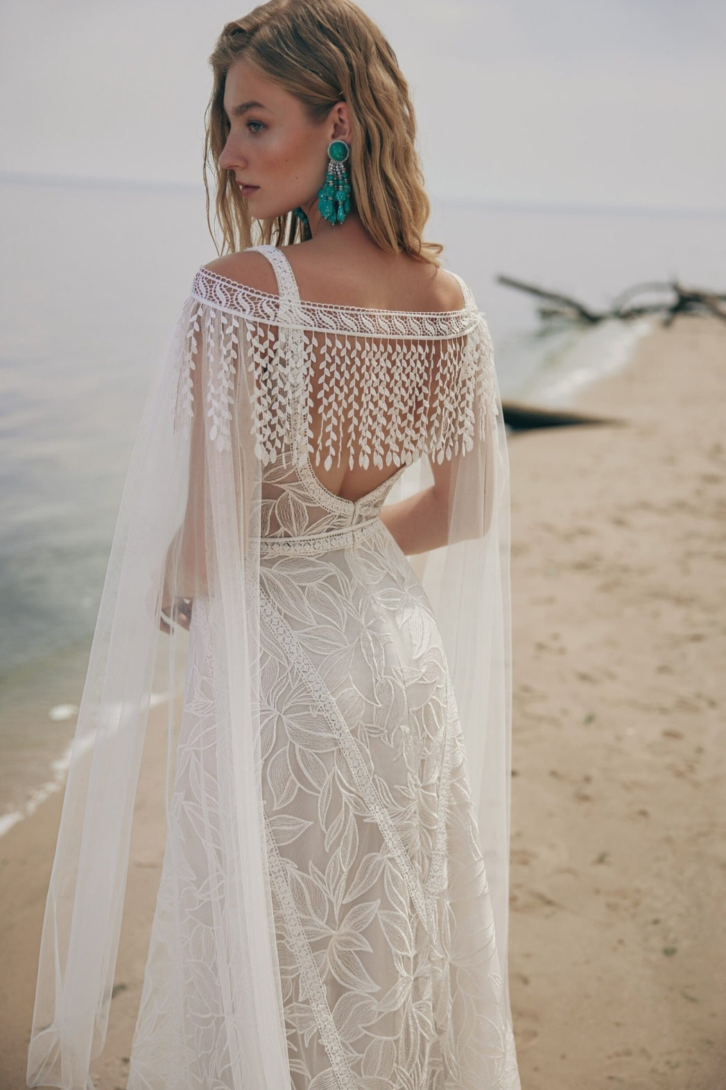 Woman in a white lace dress with a sheer overlay on a beach.