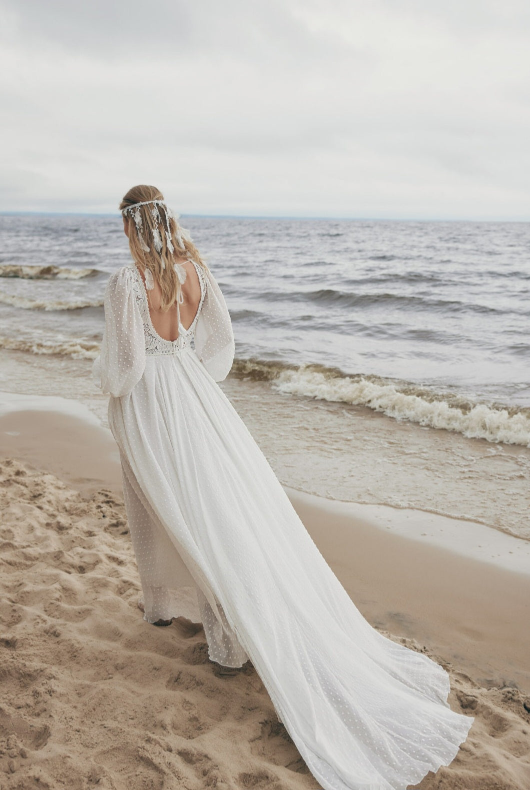 Woman in a long white dress standing on a beach with ocean waves in the background