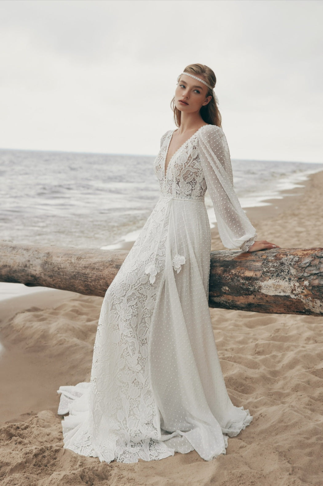 Woman in a lace wedding dress standing on a beach with ocean in the background