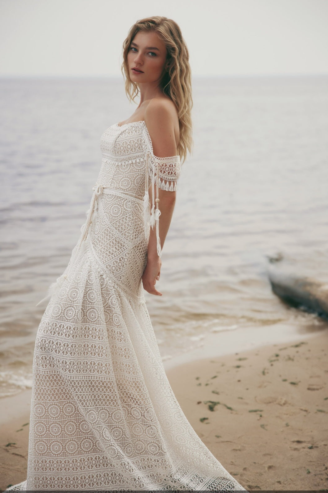 Woman in a white lace dress standing on a beach with ocean waves in the background
