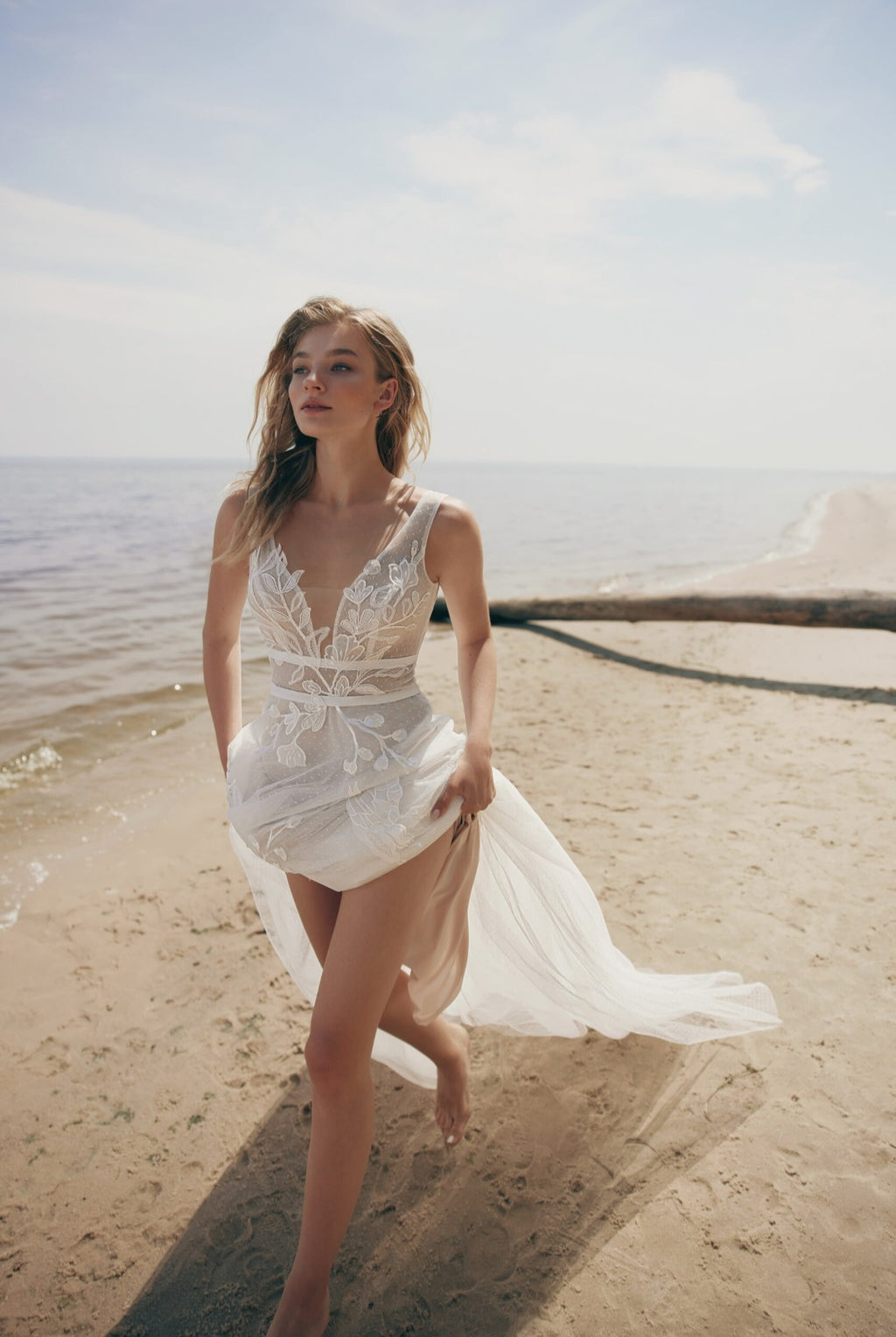 Woman in a white lace dress standing on a sandy beach with ocean in the background