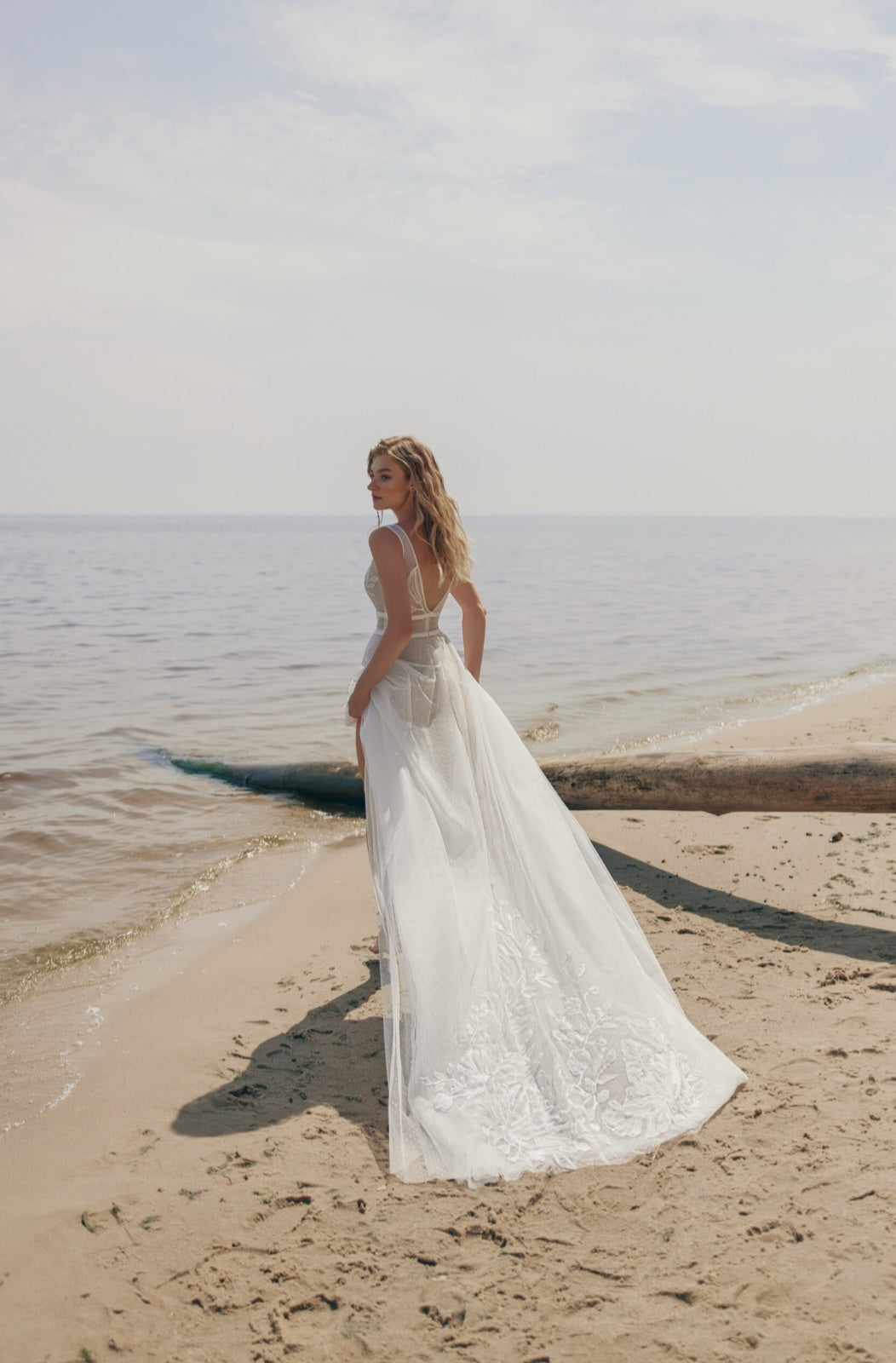 Woman in a white wedding dress standing on a beach with ocean in the background