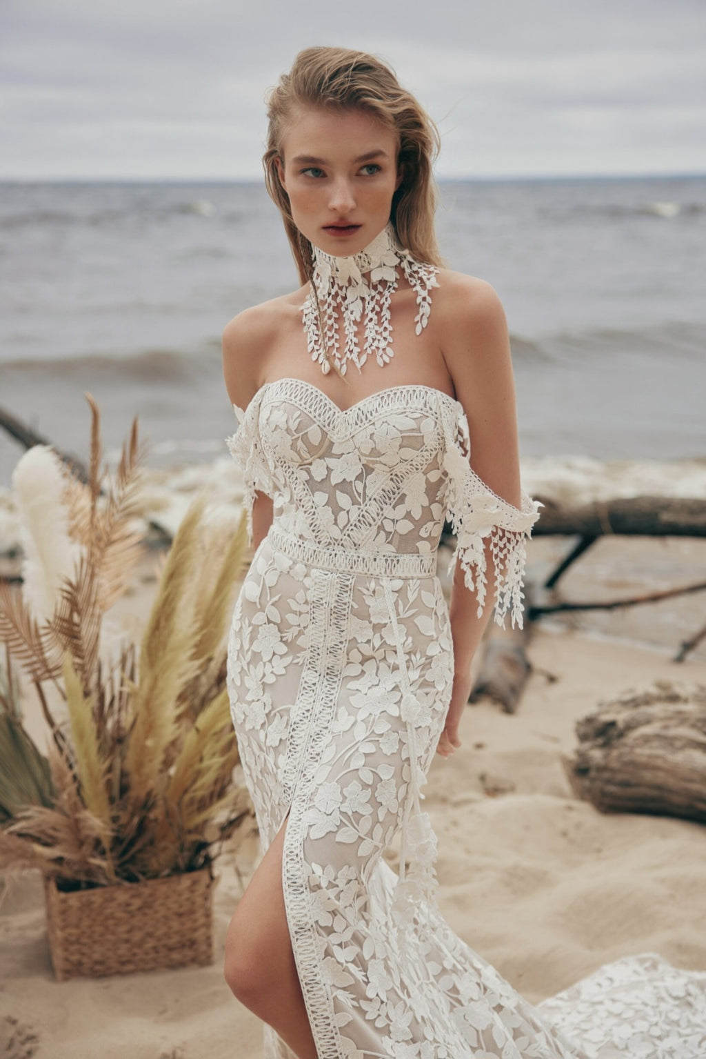 Woman in a white lace dress standing on a beach with ocean in the background
