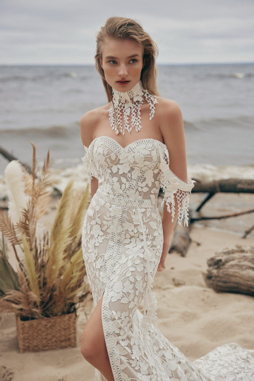 Woman in a white lace dress standing on a beach with ocean in the background