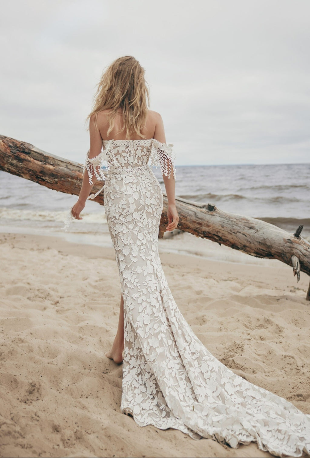 Woman in a lace dress standing on a beach with a log behind her