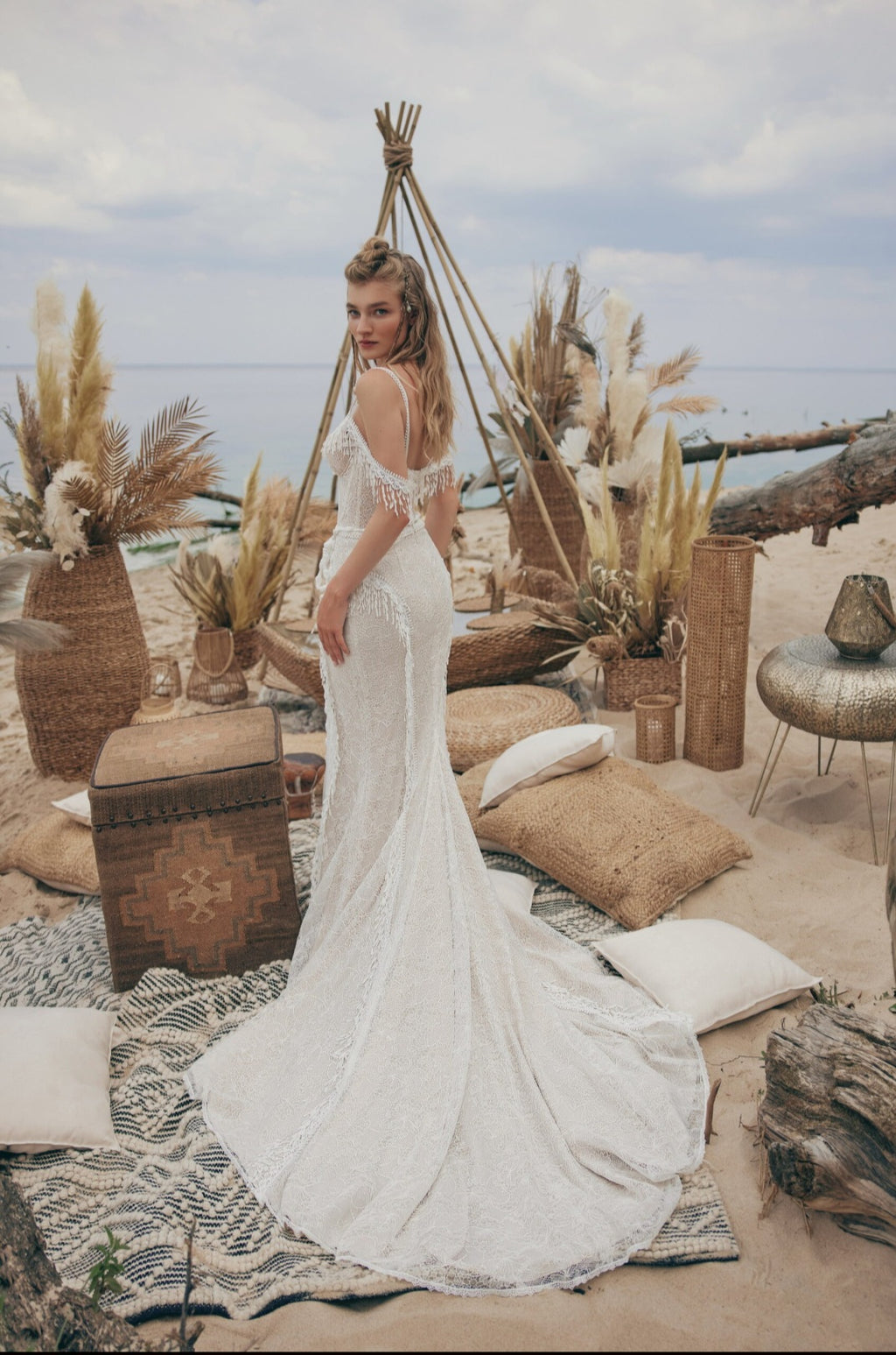 Woman in a white dress standing in a rustic outdoor setting with plants and wooden elements.