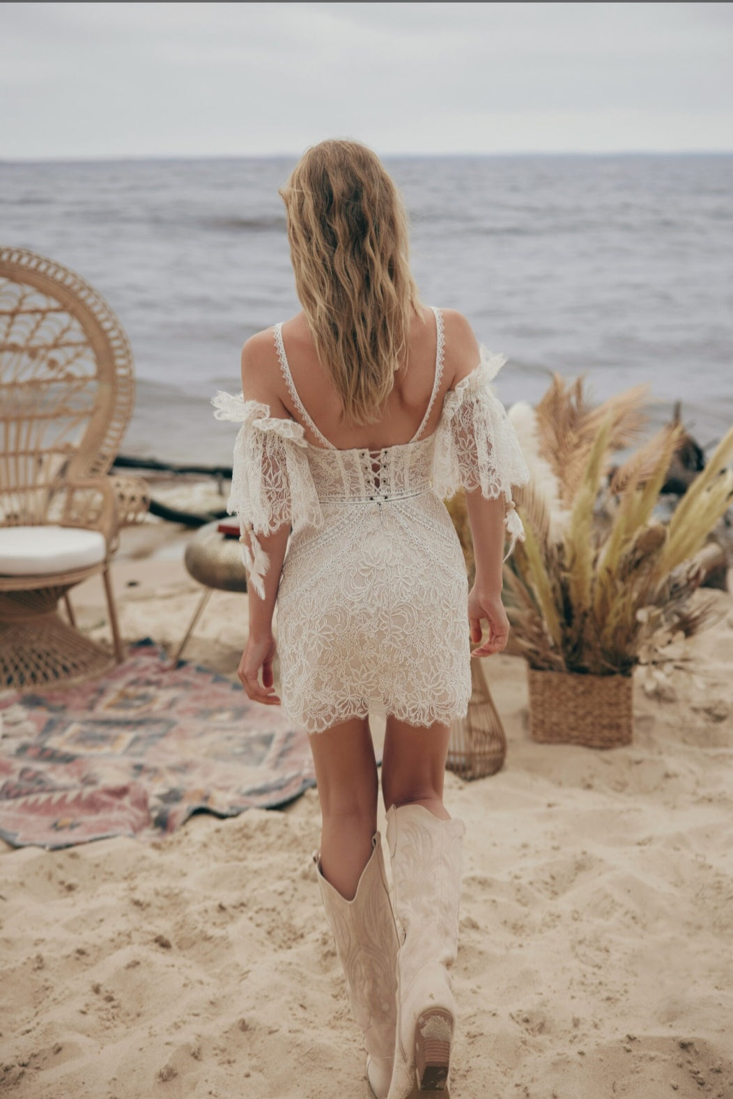 Woman in a white lace dress walking on a beach with ocean view