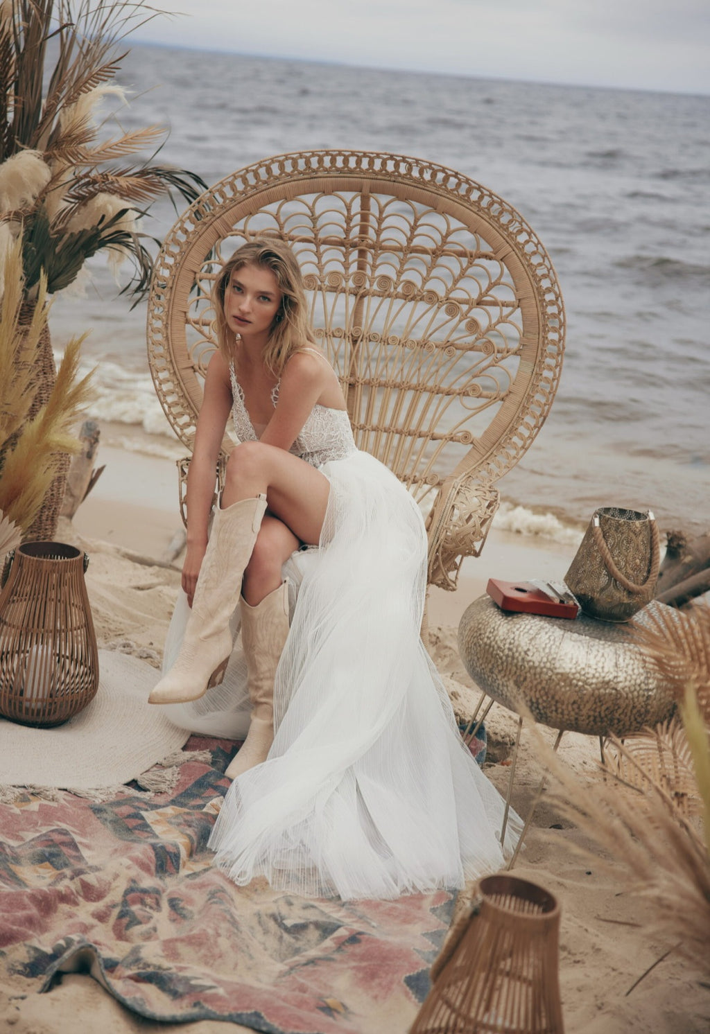Woman in a white dress sitting on a wicker chair by the ocean.