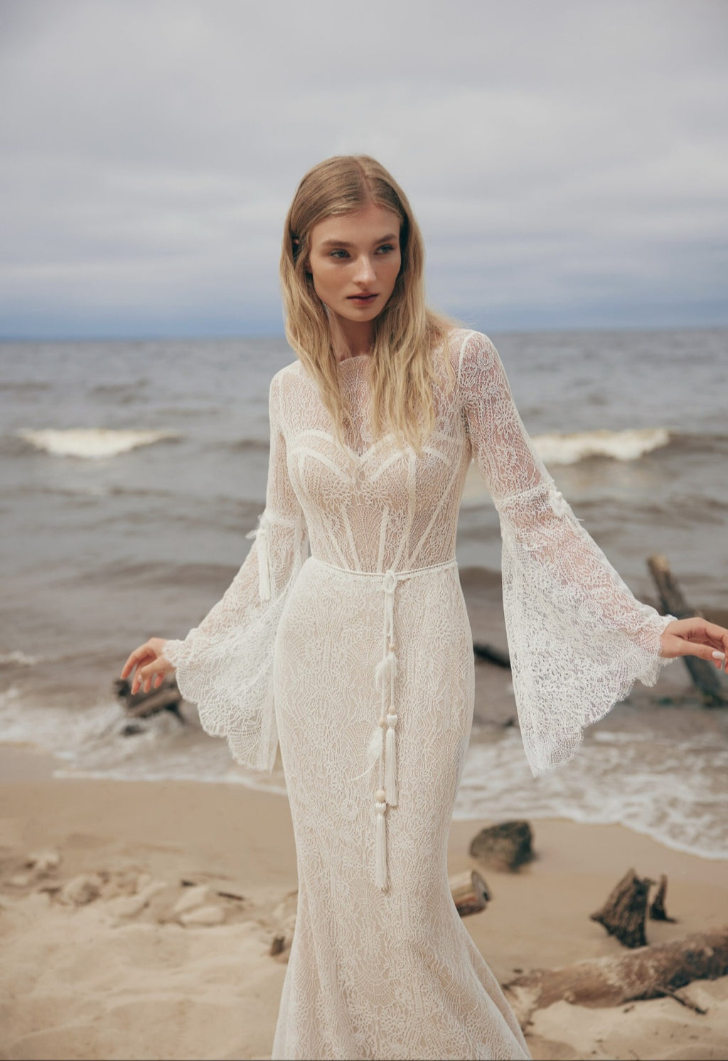 Woman in a white lace dress standing on a beach with ocean waves in the background
