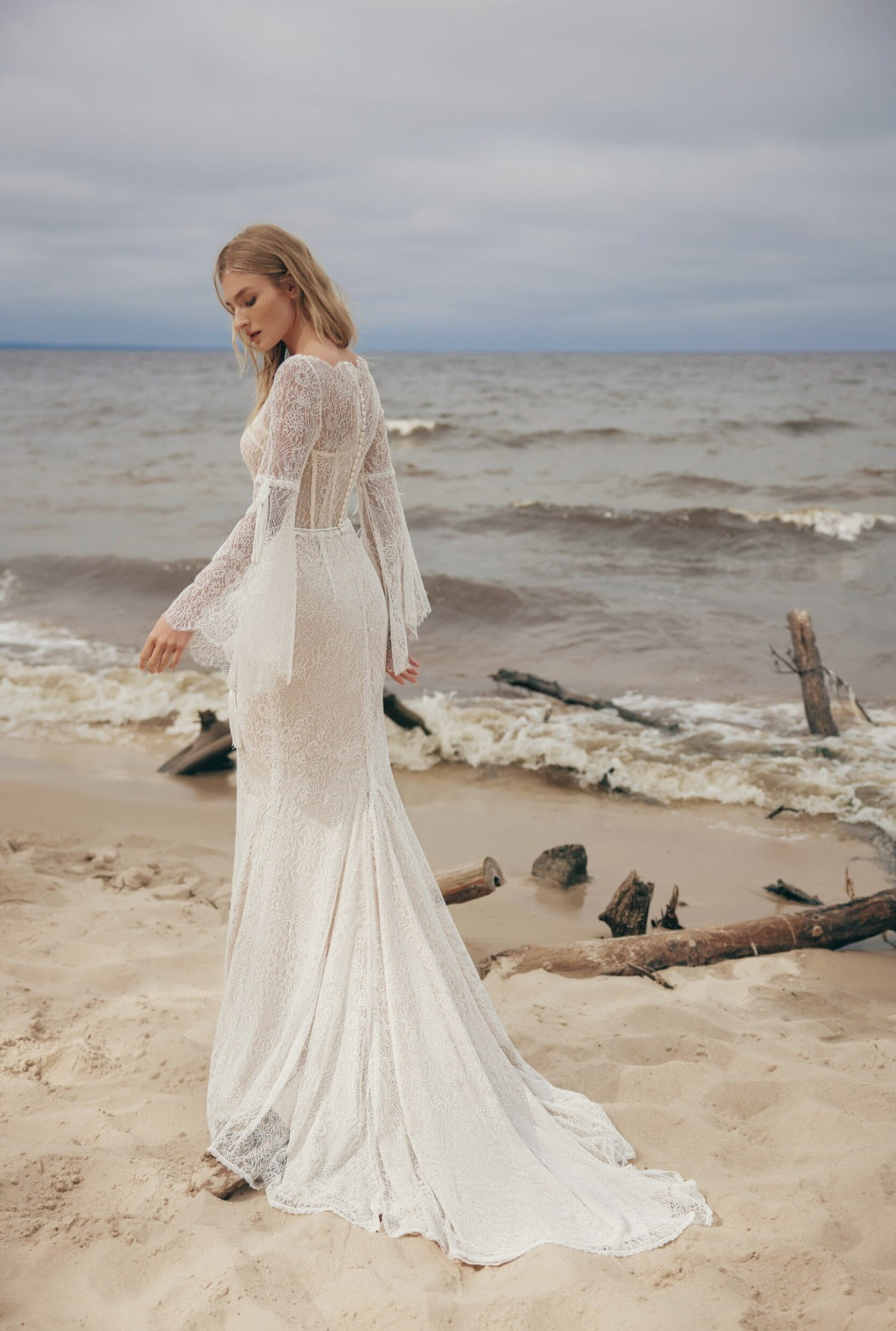Woman in a white lace dress standing on a beach with ocean waves in the background