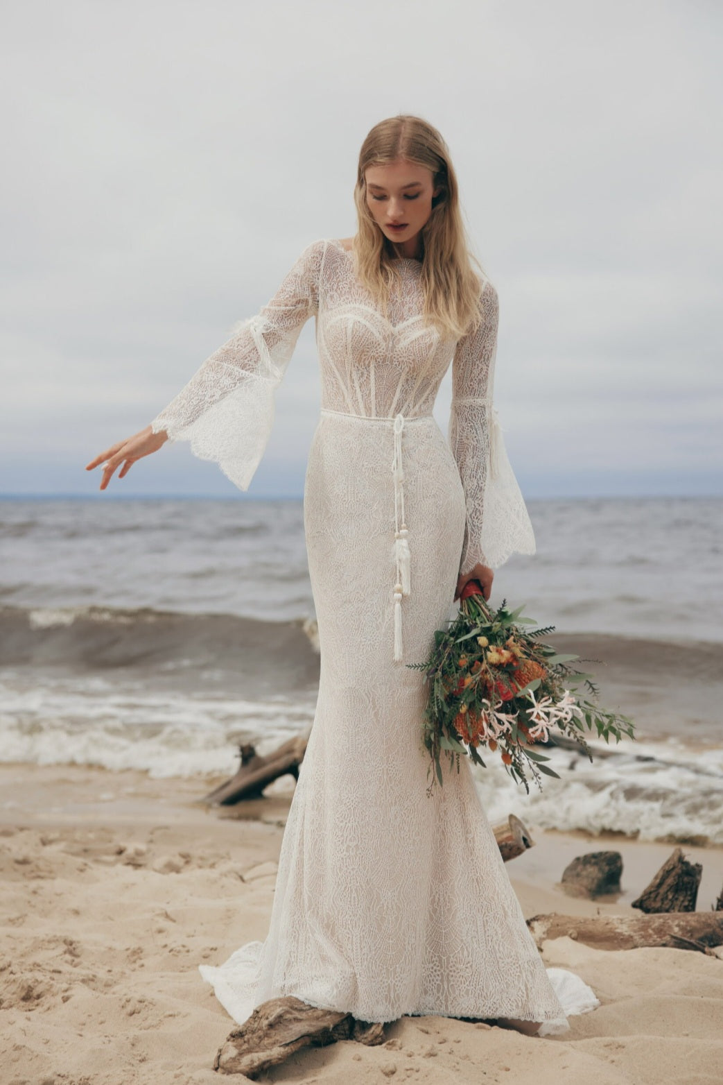 Woman in a white lace dress holding a bouquet on a beach