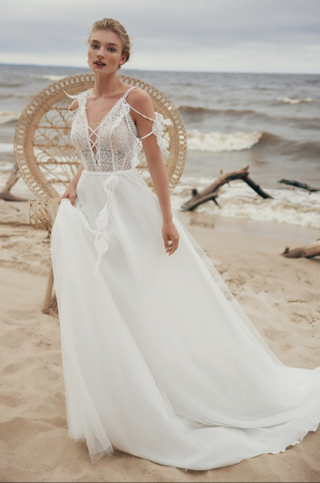 Woman in a white wedding dress standing on a beach with ocean waves in the background