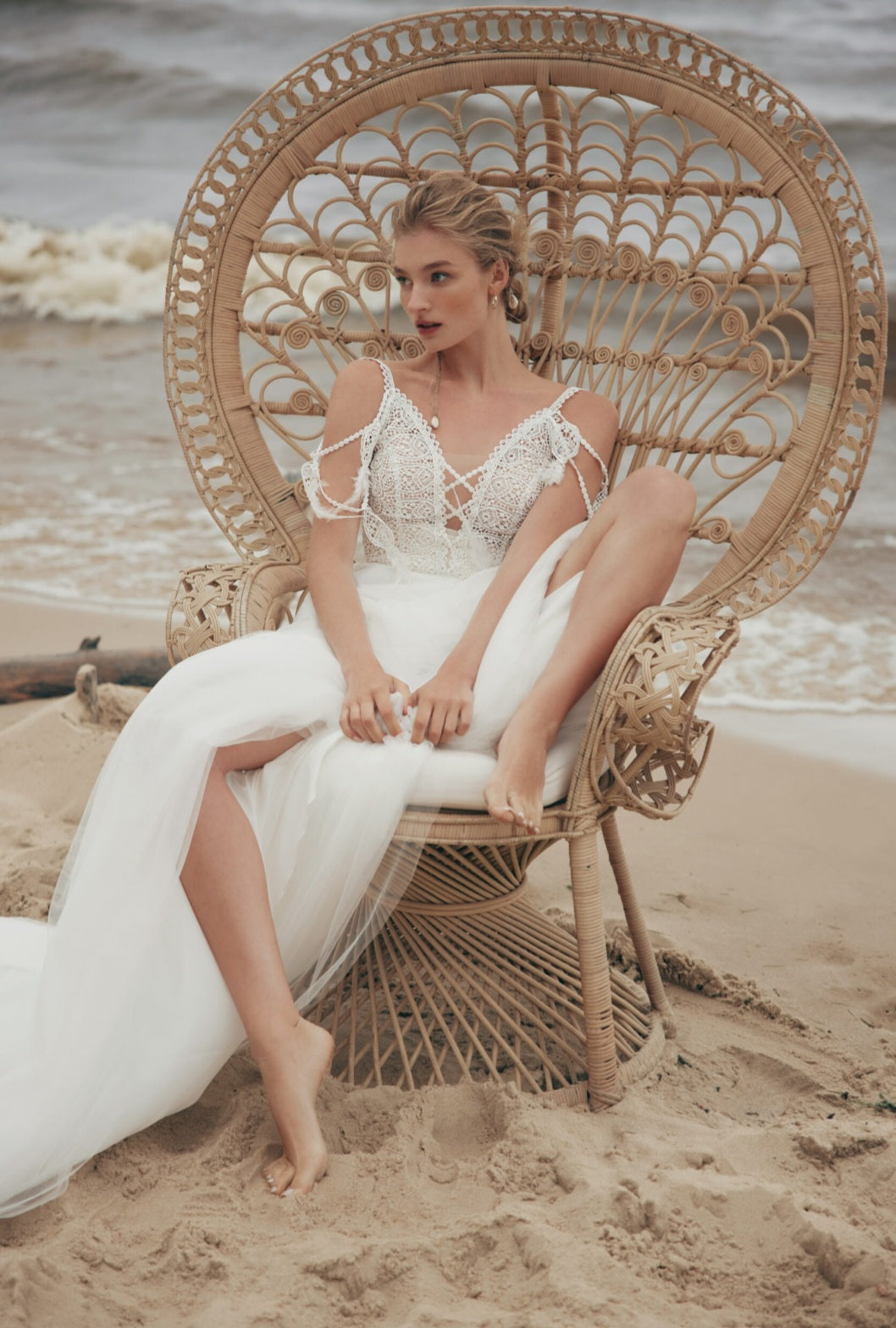 Woman in a white dress sitting on a wicker chair by the beach.