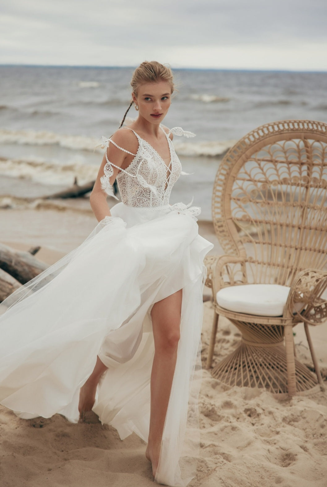 Woman in a white dress standing on a beach with wicker chair and ocean view