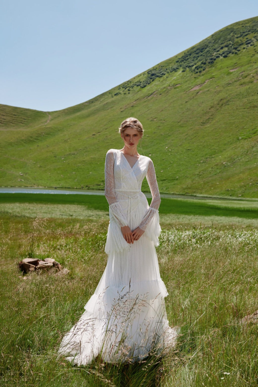 Woman in a white dress standing in a grassy field with rolling hills in the background