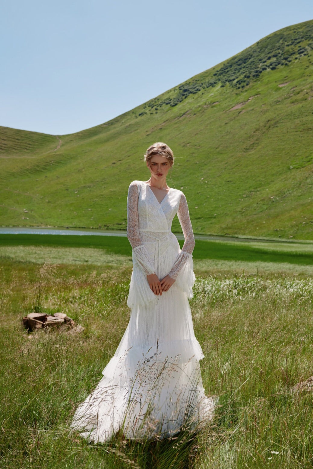 Woman in a white dress standing in a grassy field with rolling hills in the background