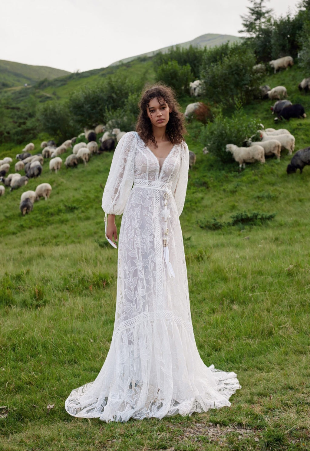 Woman in a white dress standing in a field with sheep