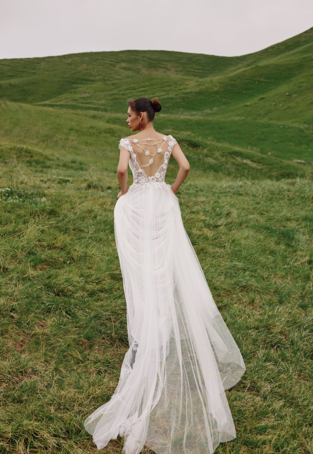 Woman in a white wedding dress standing in a grassy field with rolling hills in the background