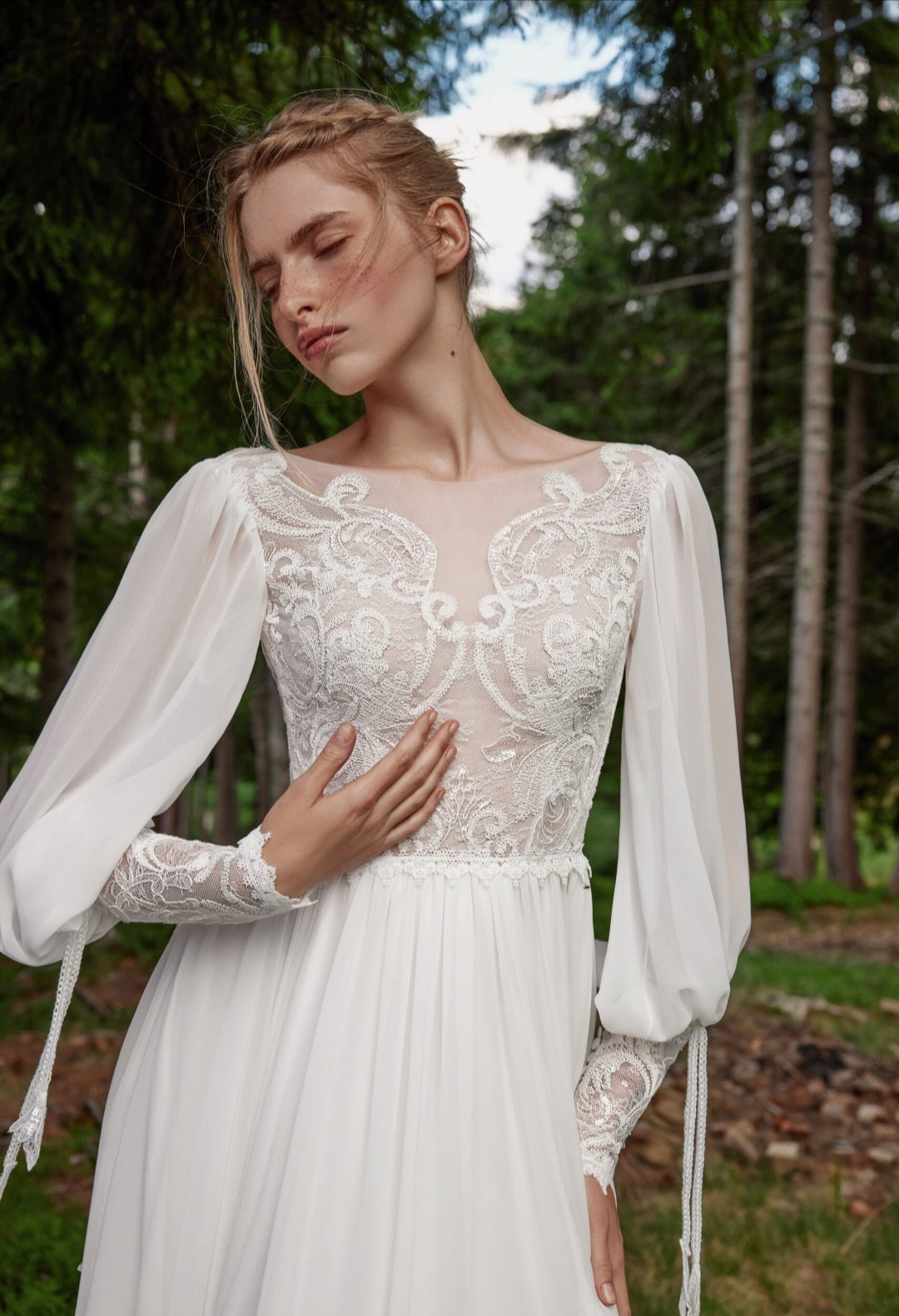 Woman wearing a white lace dress with sheer sleeves in a forest setting
