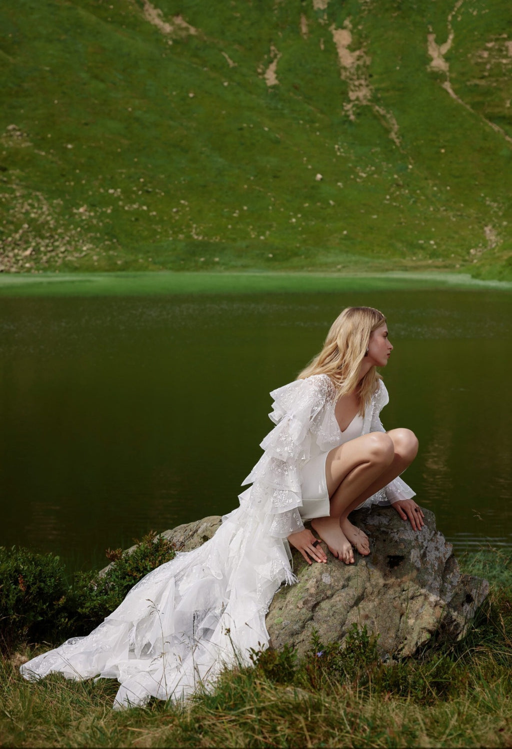 Woman in a white dress sitting on a rock by a lake