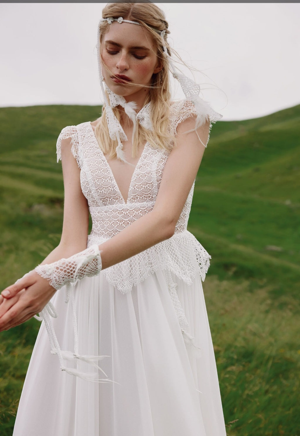 Woman in a white lace wedding dress standing in a grassy field