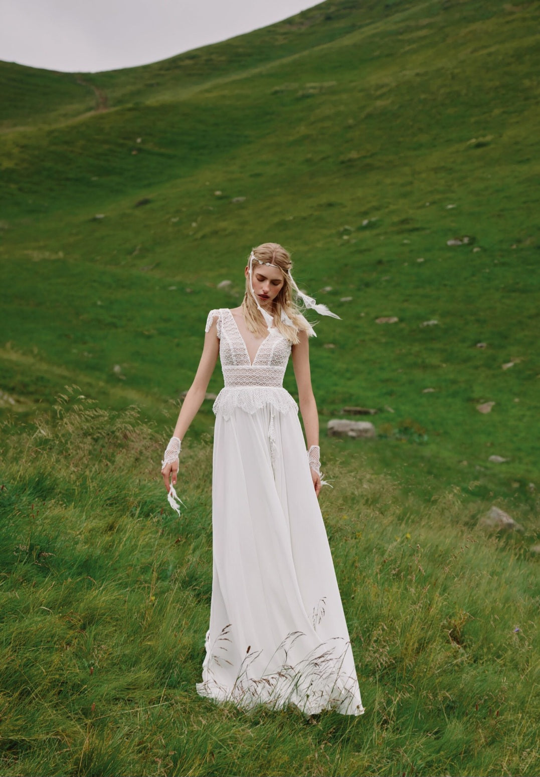Woman in a white dress standing in a grassy field with hills in the background