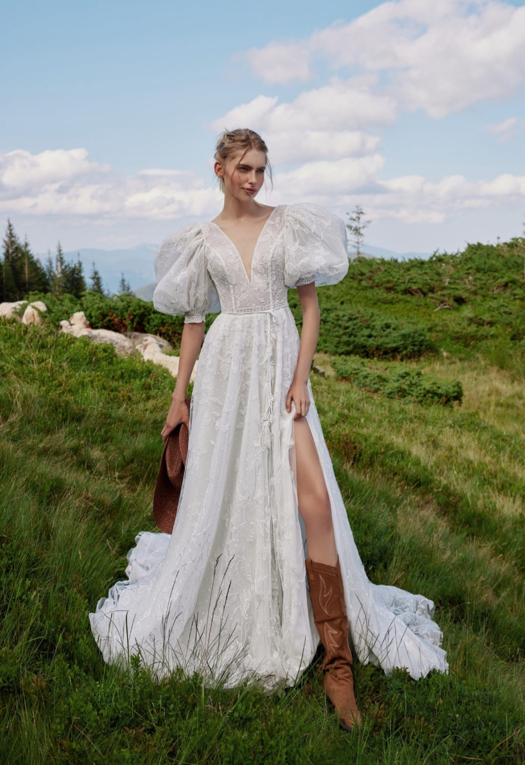 Woman in a white wedding dress with puffed sleeves and a slit skirt standing in a grassy field.