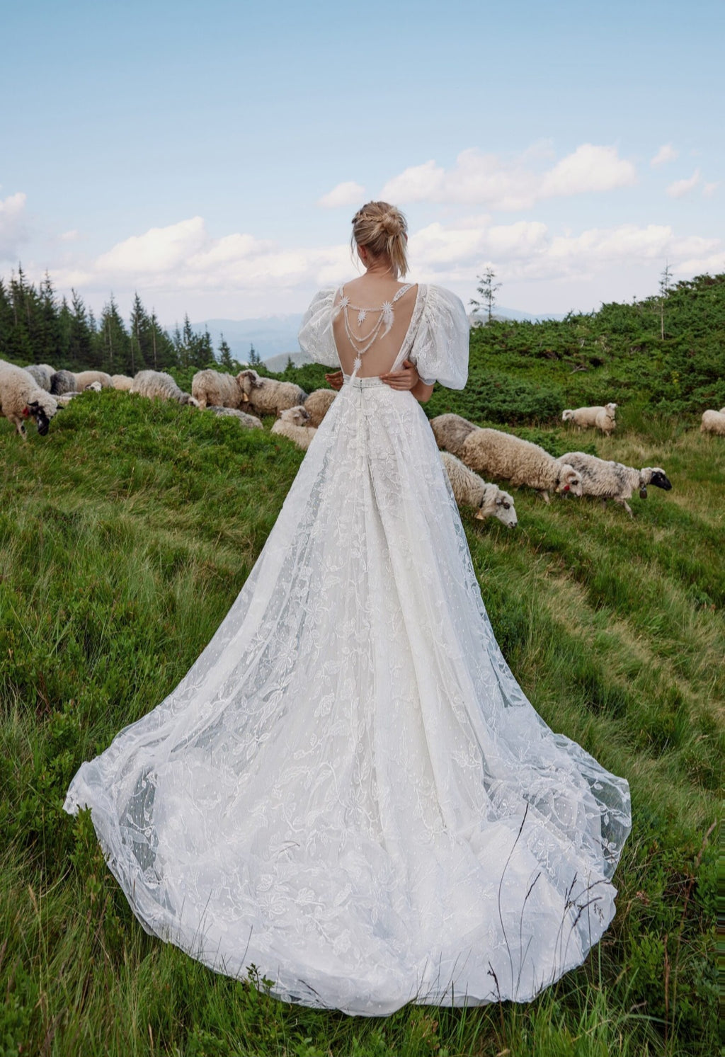 Woman in a white lace wedding dress standing in a field with sheep