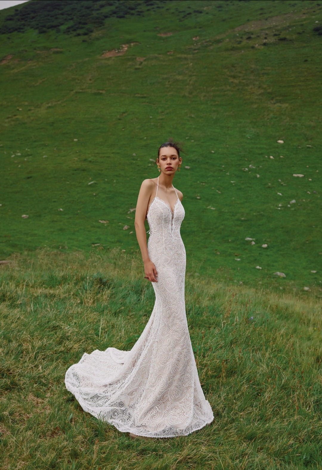 Woman in a white lace wedding dress standing in a grassy field