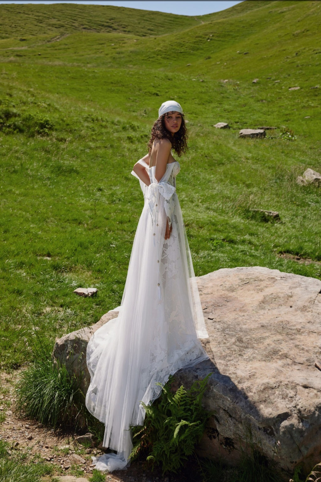 Woman in a white dress standing on a rock in a grassy field